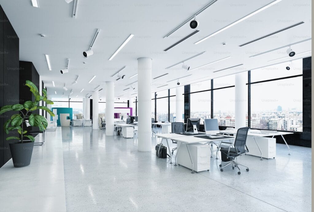 Un immeuble de bureaux moderne en verre avec des fenêtres reflétant le ciel bleu clair, entouré de verdure, symbolisant la durabilité et l'innovation en architecture urbaine.