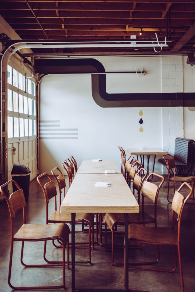Salle de réunion au design industriel avec des chaises en métal et bois autour de longues tables claires dans un espace lumineux et original